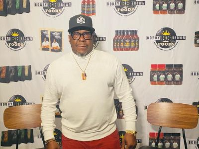 Bobby Brown is wearing a white tee, red pant, a chain and a black cap in the picture.